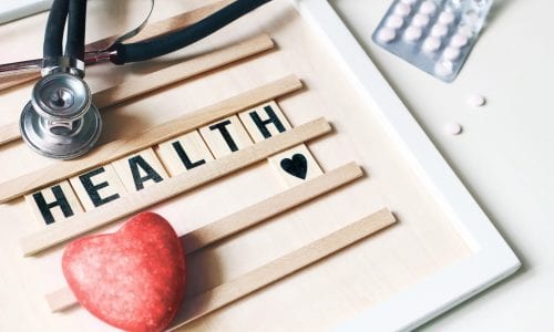 Closeup of red heart stone, stethoscope, wooden letter board and pills on white table background. Health care, medical examination. Heart insurance and cardiology concept. World Health day.